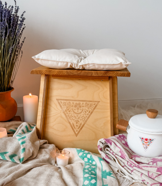 A wooden stool with a cushion, candles, and lavender on a textured surface.